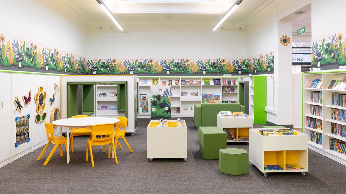 Kilburn Library children's area from a front view showing a white table and yellow chairs and lots of nature inspired decorative design motifs