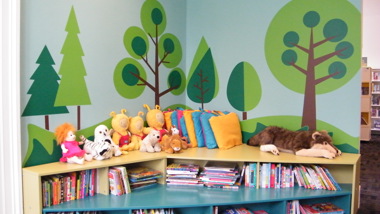 A brightly decorated wall with a woodland mural above child friendly book shelves