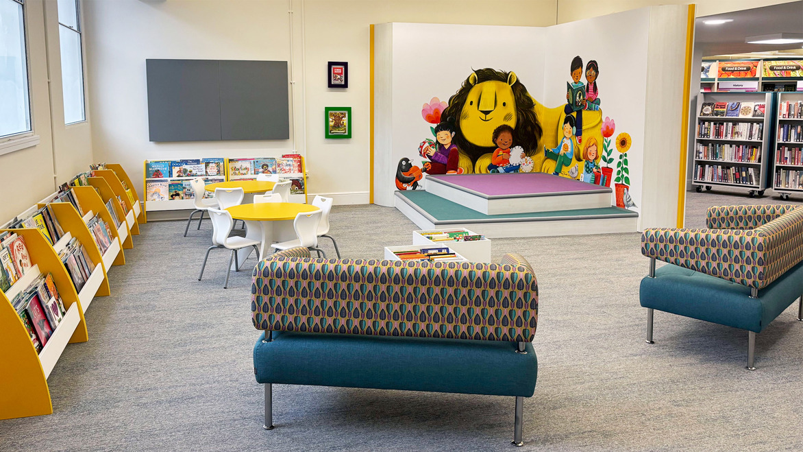 Under Fives Area with a giant book reading nook in front of an illustrated lion mural